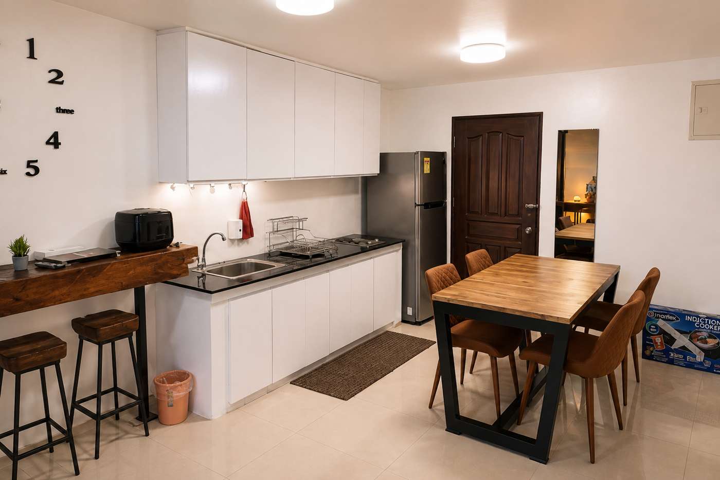 Bright shared kitchen and dining area at Mayumi Lodge with a wooden table, bar stools, refrigerator and induction cooker
