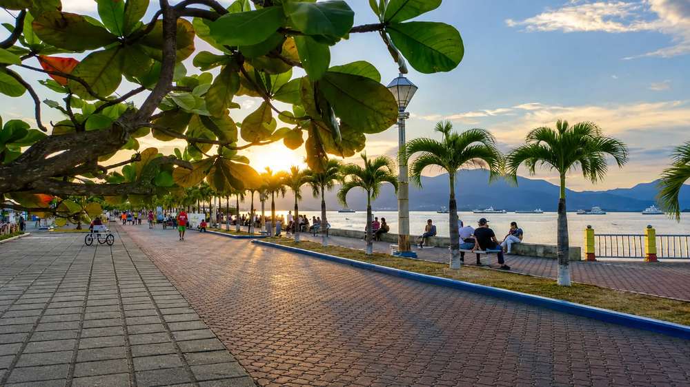 Palm-lined baywalk promenade in Puerto Princesa at sunset with people sitting on benches facing the water