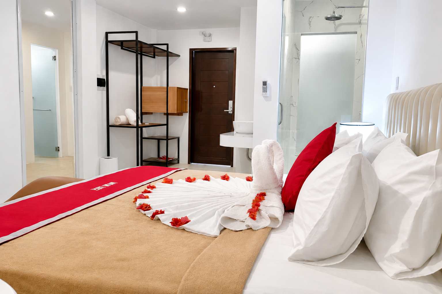 Mayumi Lodge room with a red runner, rose petals and a folded towel display on the bed, beside a walk-in shower