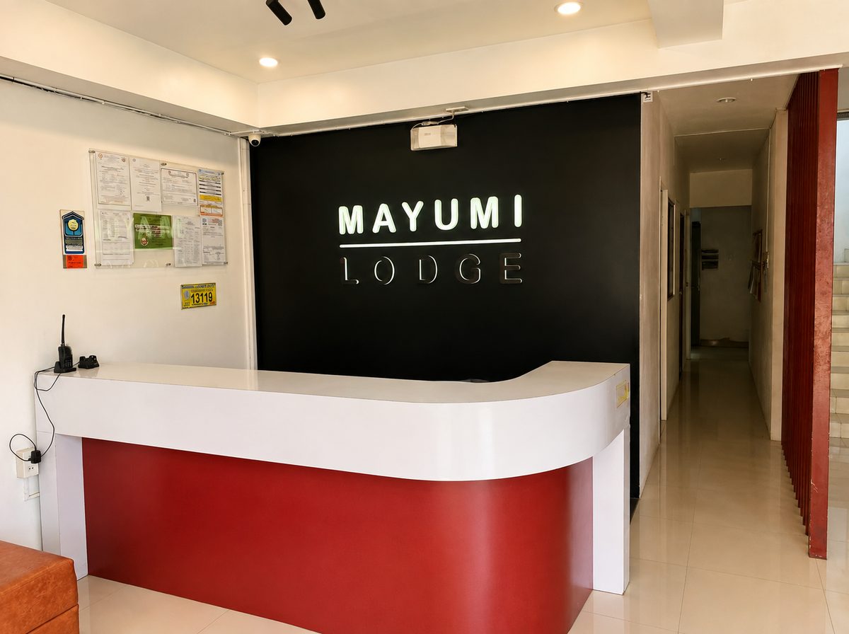Mayumi Lodge reception counter in red and white beneath the illuminated Mayumi Lodge sign on a black wall