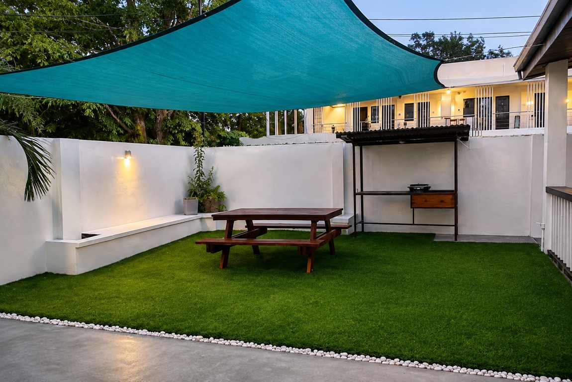 Shaded lawn courtyard at Mayumi Lodge with a wooden picnic table, grill station and white garden walls