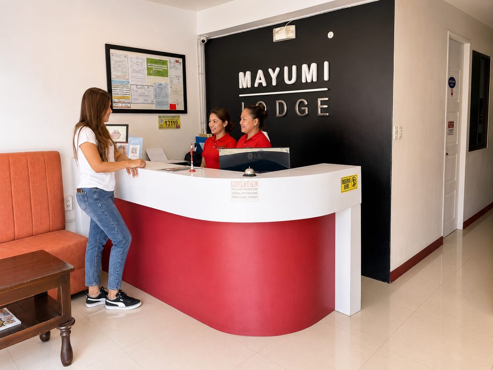 Guest speaking with two Mayumi Lodge front desk staff in red polo shirts at the red and white reception counter
