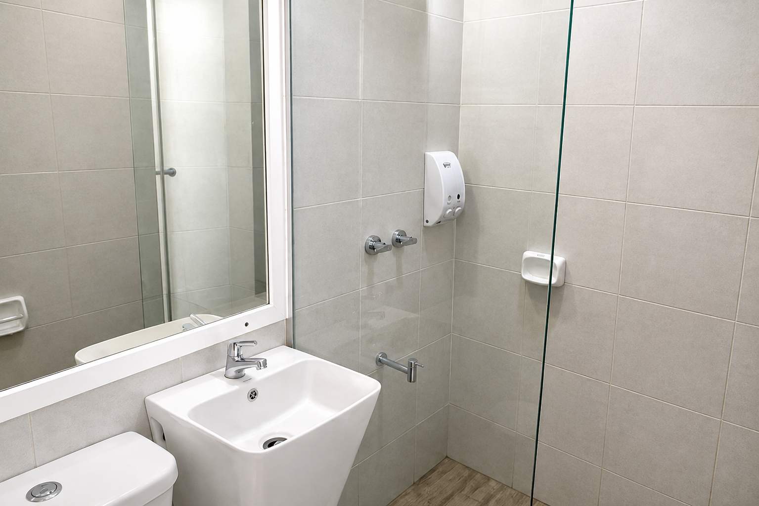 Private tiled bathroom at Mayumi Lodge with a glass shower screen, basin, mirror and wall soap dispenser